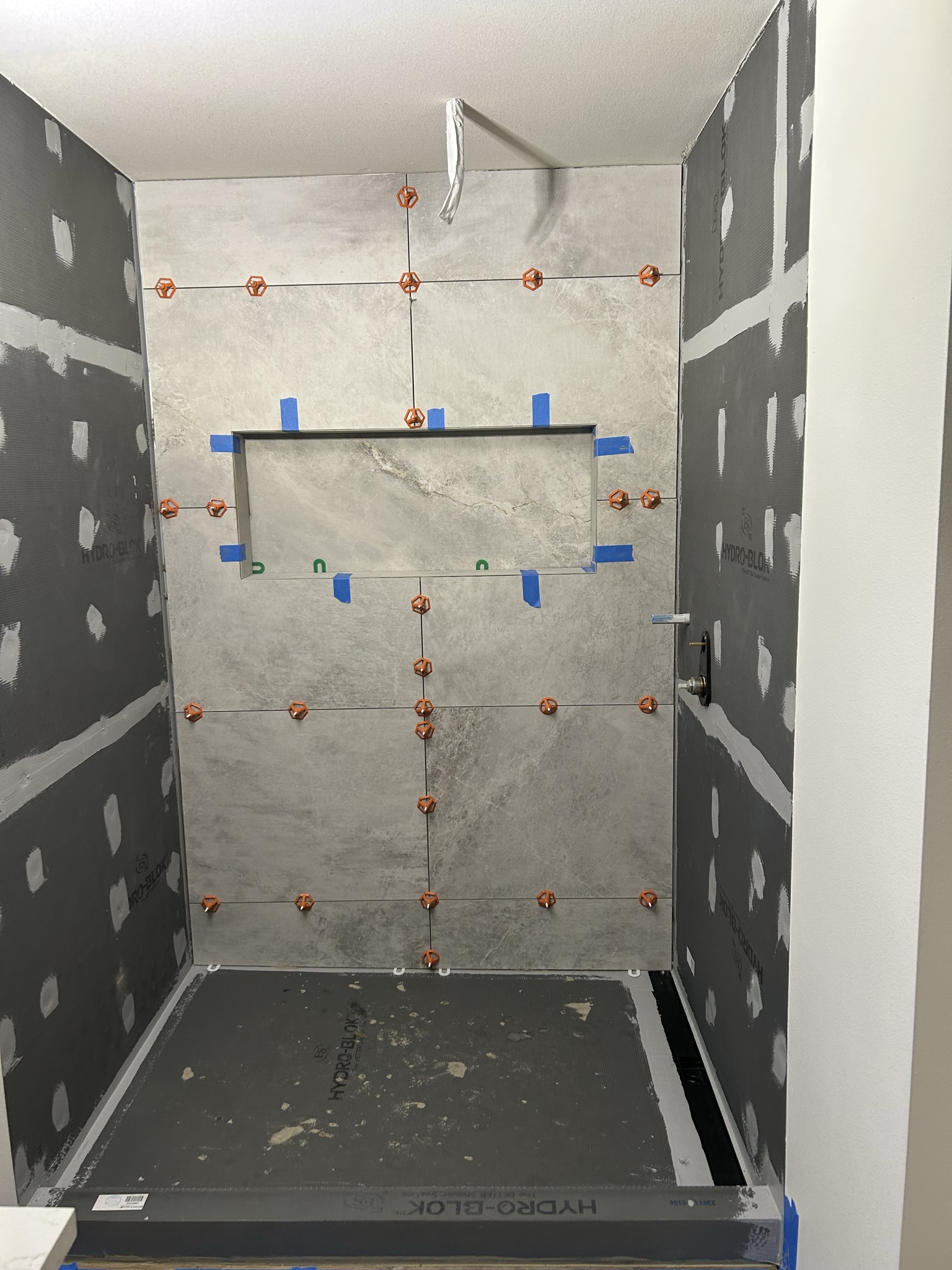 Large-format gray tile being laid out around the shower niche