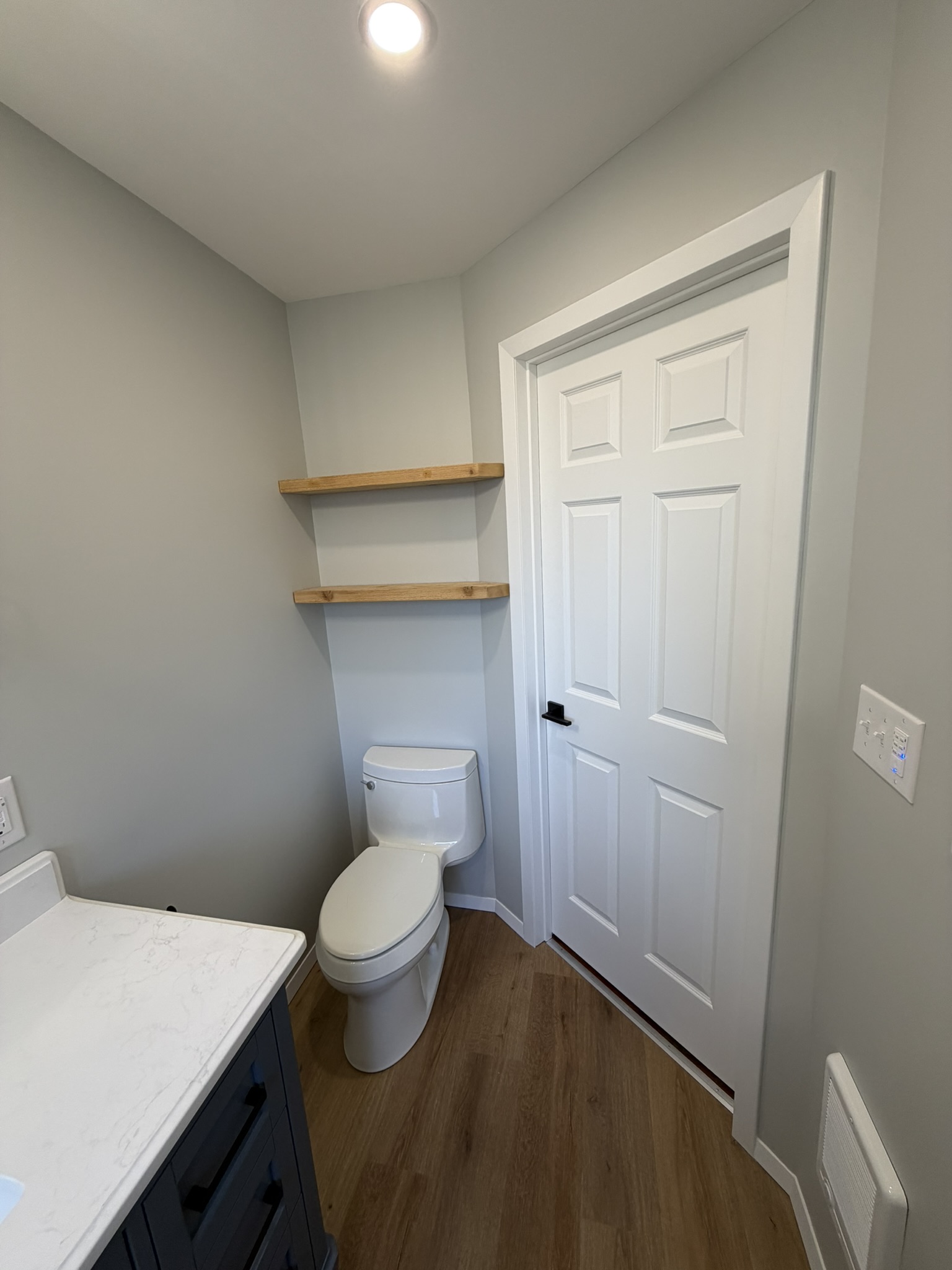 Finished toilet area with new flooring, trim, and wood shelves